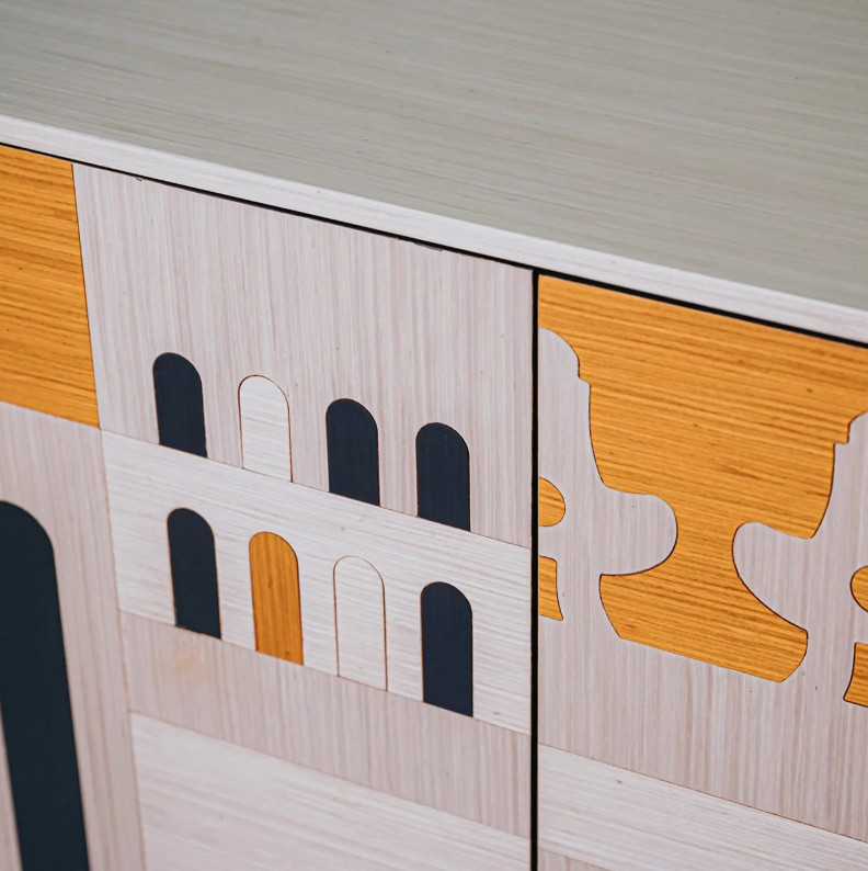 Dettaglio del frontale di una madia in legno con intarsi geometrici che richiamano forme architettoniche ad arco e sagome stilizzate.