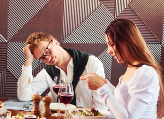 Una coppia seduta a un tavolo in un ristorante con una parete decorata da pannelli fonoassorbenti geometrici.