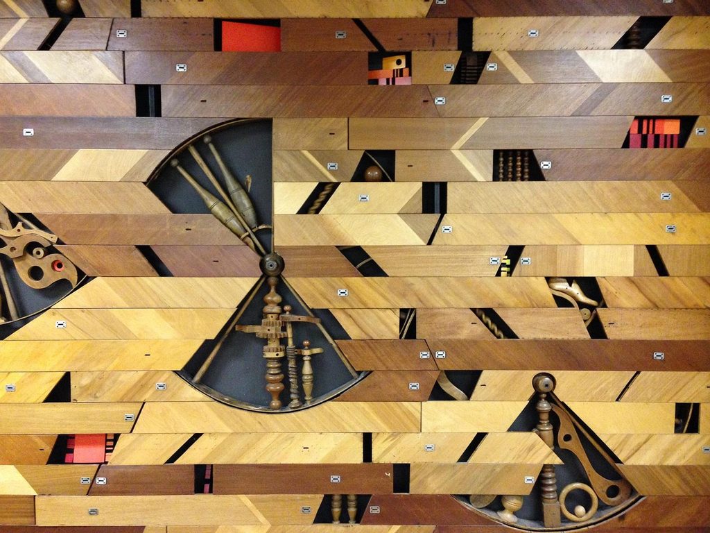 Dettaglio di una parete in legno composta da listelli disposti in diagonale con inserti decorativi e meccanismi in legno a vista.